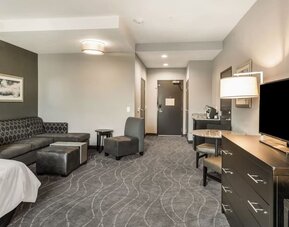Spacious guest room lounge area featuring sofa seating, armchairs, television, dining space, and modern furnishings at Holiday Inn & Suites Silicon Valley - Milpitas.