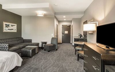 Spacious guest room lounge area featuring sofa seating, armchairs, television, dining space, and modern furnishings at Holiday Inn & Suites Silicon Valley - Milpitas.