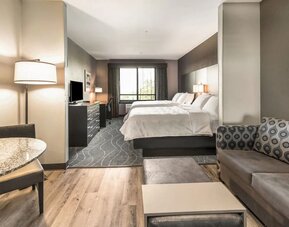 Spacious suite featuring two beds, a separate lounge area with sofa seating, dining space, and contemporary furnishings at Holiday Inn & Suites Silicon Valley - Milpitas.