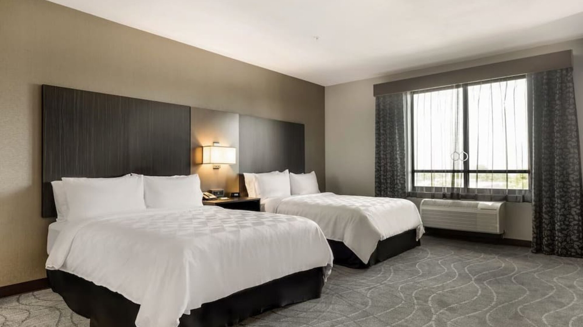 Spacious guest room featuring two beds, bedside lighting, a large window, and comfortable contemporary furnishings at Holiday Inn & Suites Silicon Valley - Milpitas.