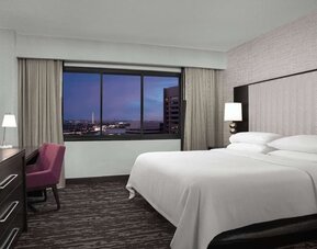Comfortable king guest room featuring a large bed, dedicated workspace, television, and expansive window with city views at Embassy Suites by Hilton Crystal City National Airport.
