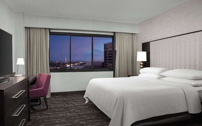 Comfortable king guest room featuring a large bed, dedicated workspace, television, and expansive window with city views at Embassy Suites by Hilton Crystal City National Airport.