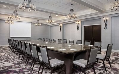 Spacious boardroom featuring a large conference table, ample seating, presentation screen, and contemporary lighting at Embassy Suites by Hilton Crystal City National Airport.