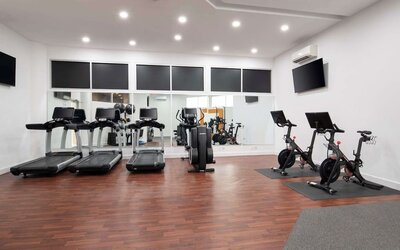 Modern fitness centre featuring treadmills, stationary bikes, cardio equipment, and wall-mounted televisions at Embassy Suites by Hilton Crystal City National Airport.