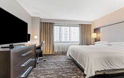 Bright king guest room featuring a comfortable bed, workspace, television, and ample natural light from a large window at Embassy Suites by Hilton Crystal City National Airport.