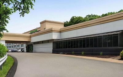 Exterior view of Wyndham Garden Pittsburgh Airport featuring the hotel entrance, covered driveway, landscaped grounds, and surrounding trees.