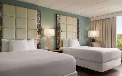 Comfortable guest room featuring two beds, modern headboards, bedside lighting, an armchair, and large window at Wyndham Garden Pittsburgh Airport.