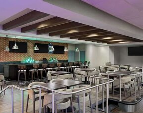 Spacious hotel bar and lounge featuring bar seating, dining tables, televisions, pendant lighting, and contemporary furnishings at Wyndham Garden Pittsburgh Airport.