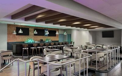 Spacious hotel bar and lounge featuring bar seating, dining tables, televisions, pendant lighting, and contemporary furnishings at Wyndham Garden Pittsburgh Airport.
