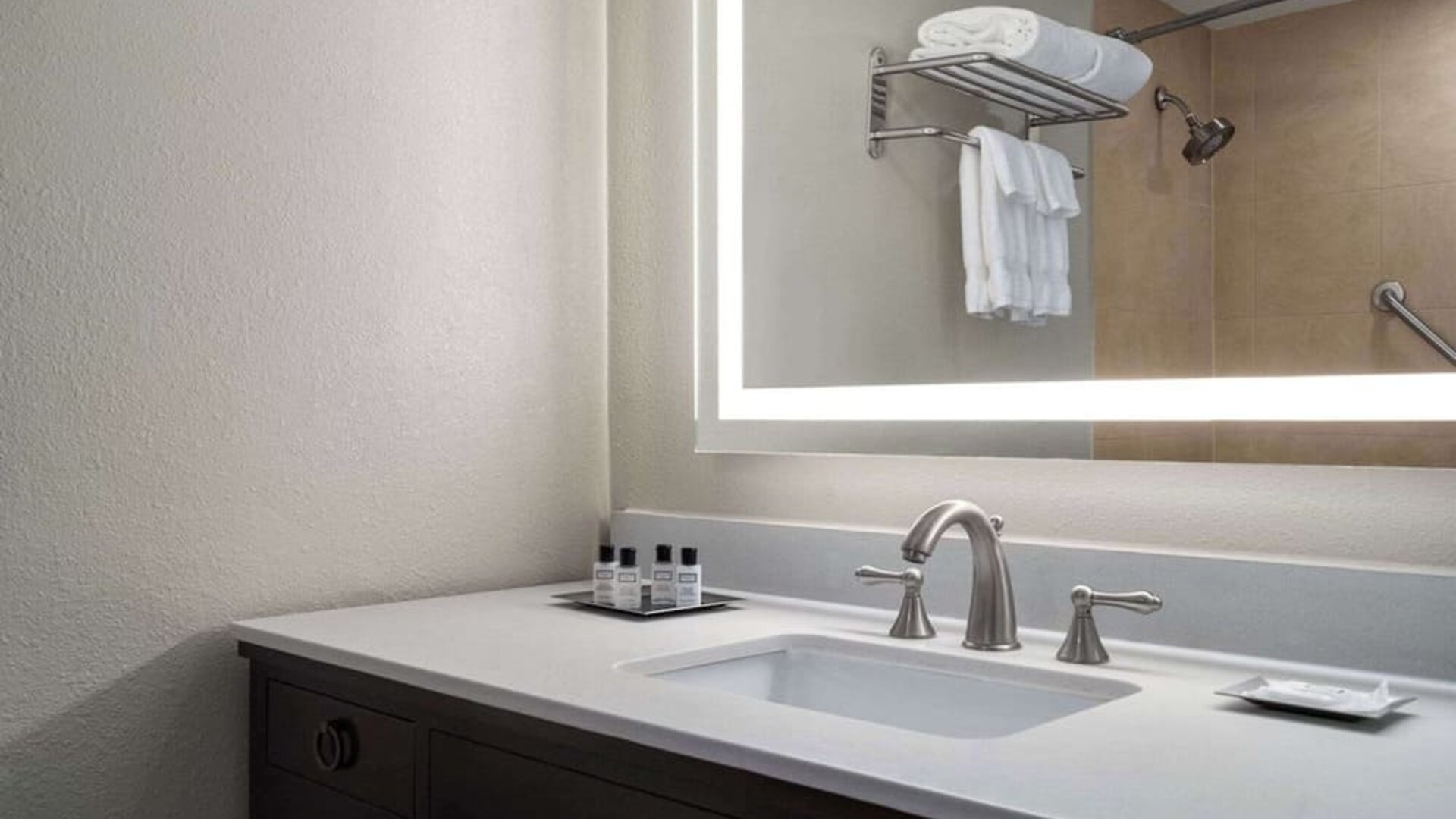 Modern guest bathroom vanity featuring a spacious countertop, illuminated mirror, toiletries, and contemporary fixtures at Wyndham Garden Pittsburgh Airport.