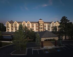 Elevated dusk view of the DoubleTree hotel exterior with illuminated entrance signage, multi-story beige facade, surrounding pine trees, dark parking area, and accessible parking spaces near the entrance.