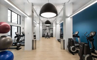 Spacious hotel fitness center with treadmills, elliptical machines, strength-training equipment, exercise balls, and weights beneath oversized pendant lights and a bright contemporary interior.