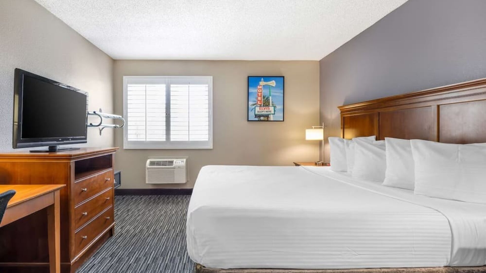 Bright king guest room featuring a large bed, television, workspace, window, and air-conditioning unit. Best Western McCarran Inn.