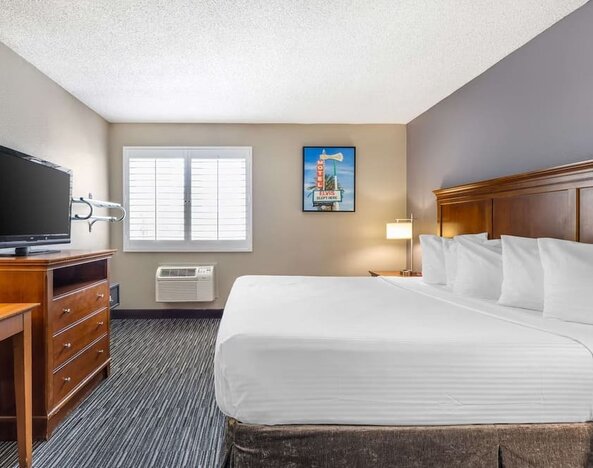 Bright king guest room featuring a large bed, television, workspace, window, and air-conditioning unit. Best Western McCarran Inn.