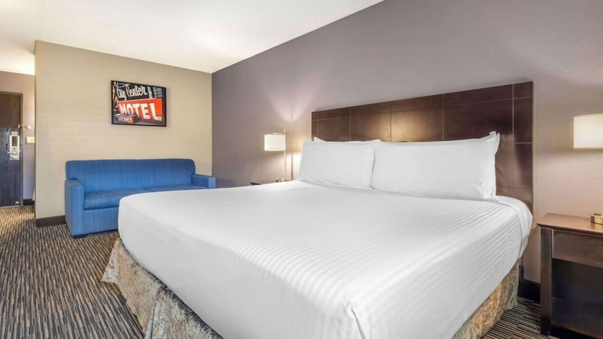 Comfortable king guest room featuring a large bed, blue sofa, bedside lighting, and contemporary décor. Best Western McCarran Inn.