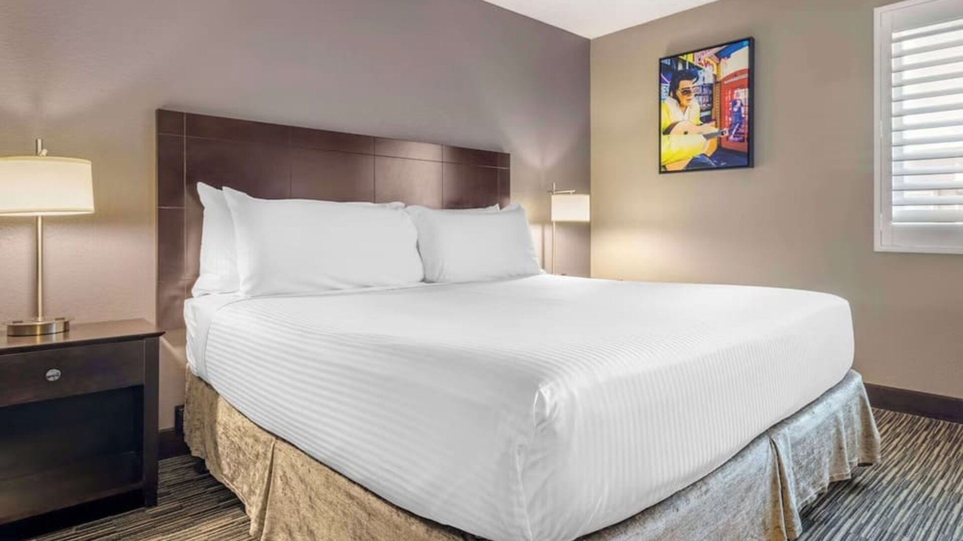 Comfortable king guest room featuring a large bed, bedside lighting, shuttered window, and colourful wall art. Best Western McCarran Inn.