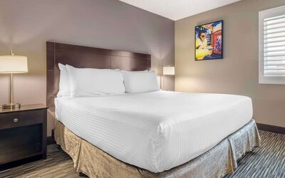 Comfortable king guest room featuring a large bed, bedside lighting, shuttered window, and colourful wall art. Best Western McCarran Inn.