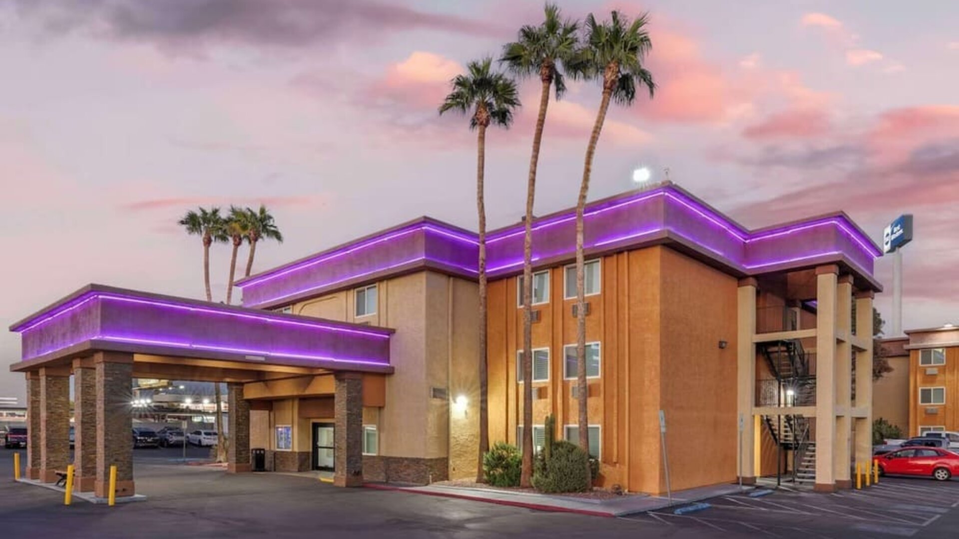 Exterior view featuring the hotel building, covered entrance, palm trees, parking area, and colourful evening sky. Best Western McCarran Inn.