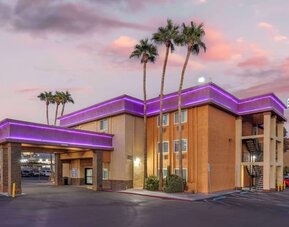 Exterior view featuring the hotel building, covered entrance, palm trees, parking area, and colourful evening sky. Best Western McCarran Inn.