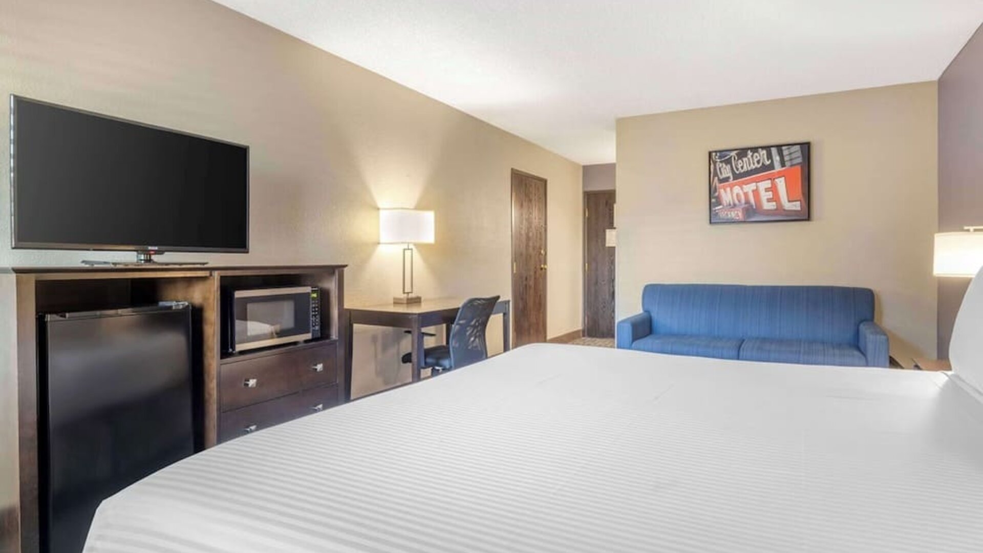 Guest room featuring a bed, blue sofa, television, mini fridge, microwave, and workspace. Best Western McCarran Inn.