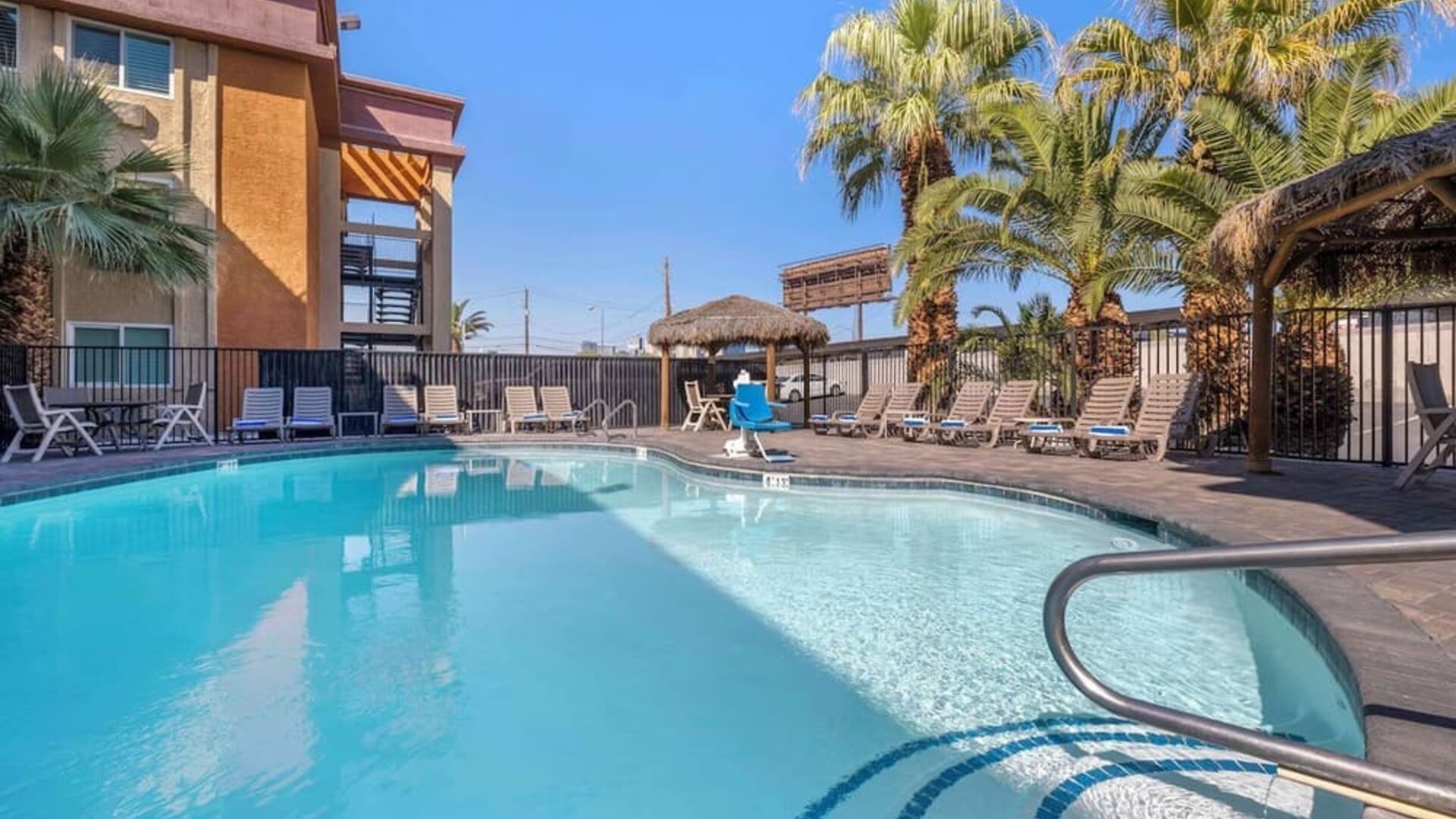 Outdoor swimming pool surrounded by sun loungers, palm trees, shaded seating areas, and tropical landscaping. Best Western McCarran Inn.