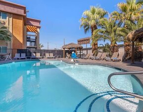 Outdoor swimming pool surrounded by sun loungers, palm trees, shaded seating areas, and tropical landscaping. Best Western McCarran Inn.