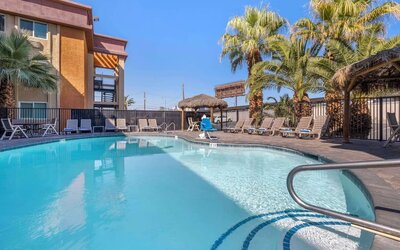 Outdoor swimming pool surrounded by sun loungers, palm trees, shaded seating areas, and tropical landscaping. Best Western McCarran Inn.