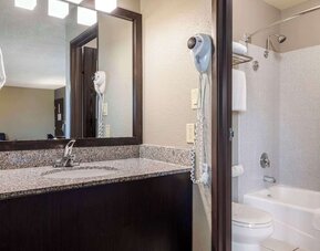 Guest bathroom featuring a granite vanity, large mirror, bathtub and shower combination, and wall-mounted hairdryer. Best Western McCarran Inn.