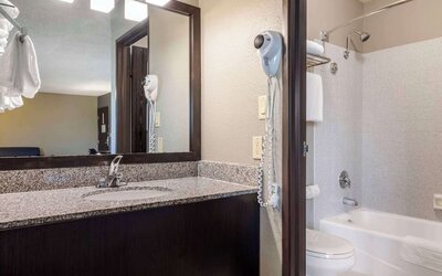 Guest bathroom featuring a granite vanity, large mirror, bathtub and shower combination, and wall-mounted hairdryer. Best Western McCarran Inn.