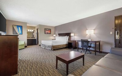 Spacious guest room featuring a bed, sofa, coffee table, workspace, and separate vanity area. Best Western McCarran Inn.