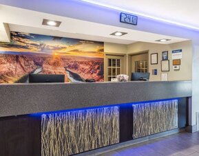 Reception desk featuring contemporary lighting, computer stations, decorative panels, and a scenic canyon mural. Best Western McCarran Inn.