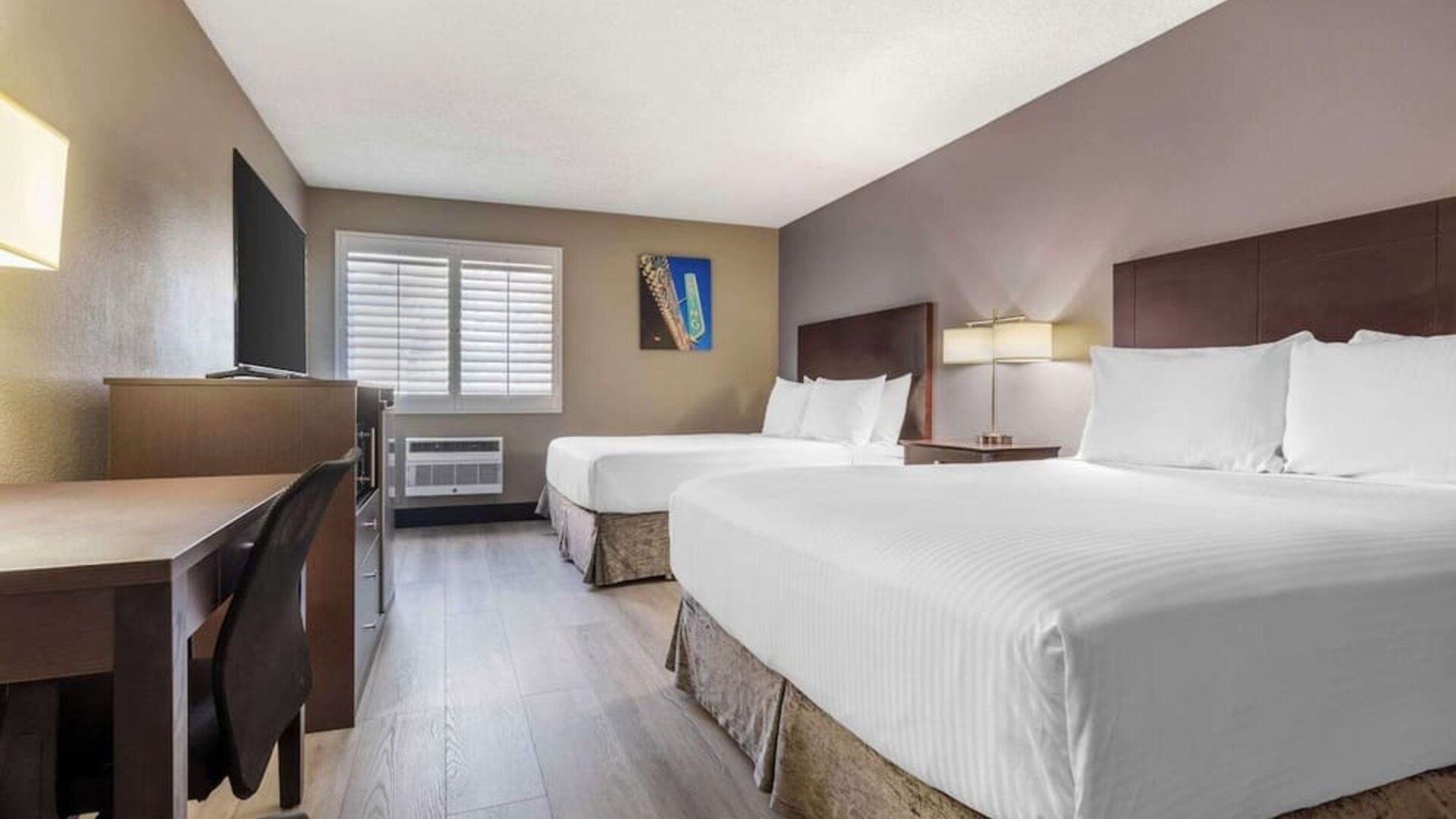 Guest room featuring two beds, workspace, television, shuttered window, and air-conditioning unit. Best Western McCarran Inn.