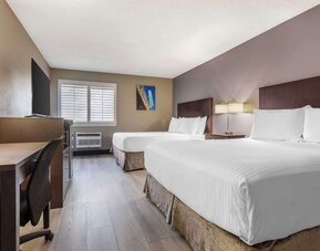 Guest room featuring two beds, workspace, television, shuttered window, and air-conditioning unit. Best Western McCarran Inn.