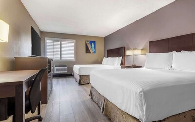 Guest room featuring two beds, workspace, television, shuttered window, and air-conditioning unit. Best Western McCarran Inn.