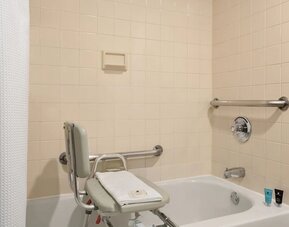 Accessible bathroom featuring a bathtub with transfer bench, grab bars, shower curtain, and bath amenities. Crowne Plaza Englewood.