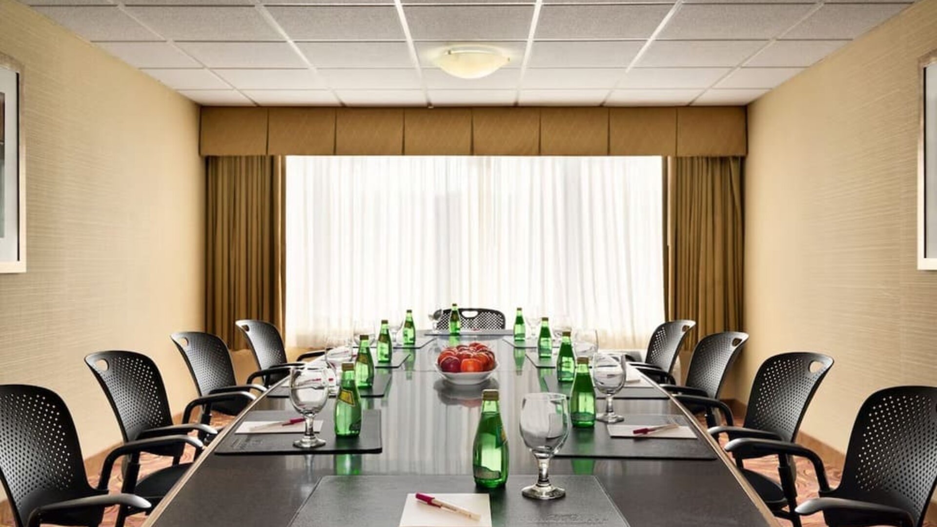 Boardroom featuring a long conference table, office chairs, bottled water, glasses, and writing pads. Crowne Plaza Englewood.