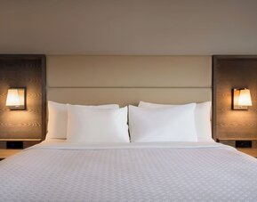 King guest room featuring a large bed with padded headboard, bedside tables, and integrated reading lights. Crowne Plaza Englewood.