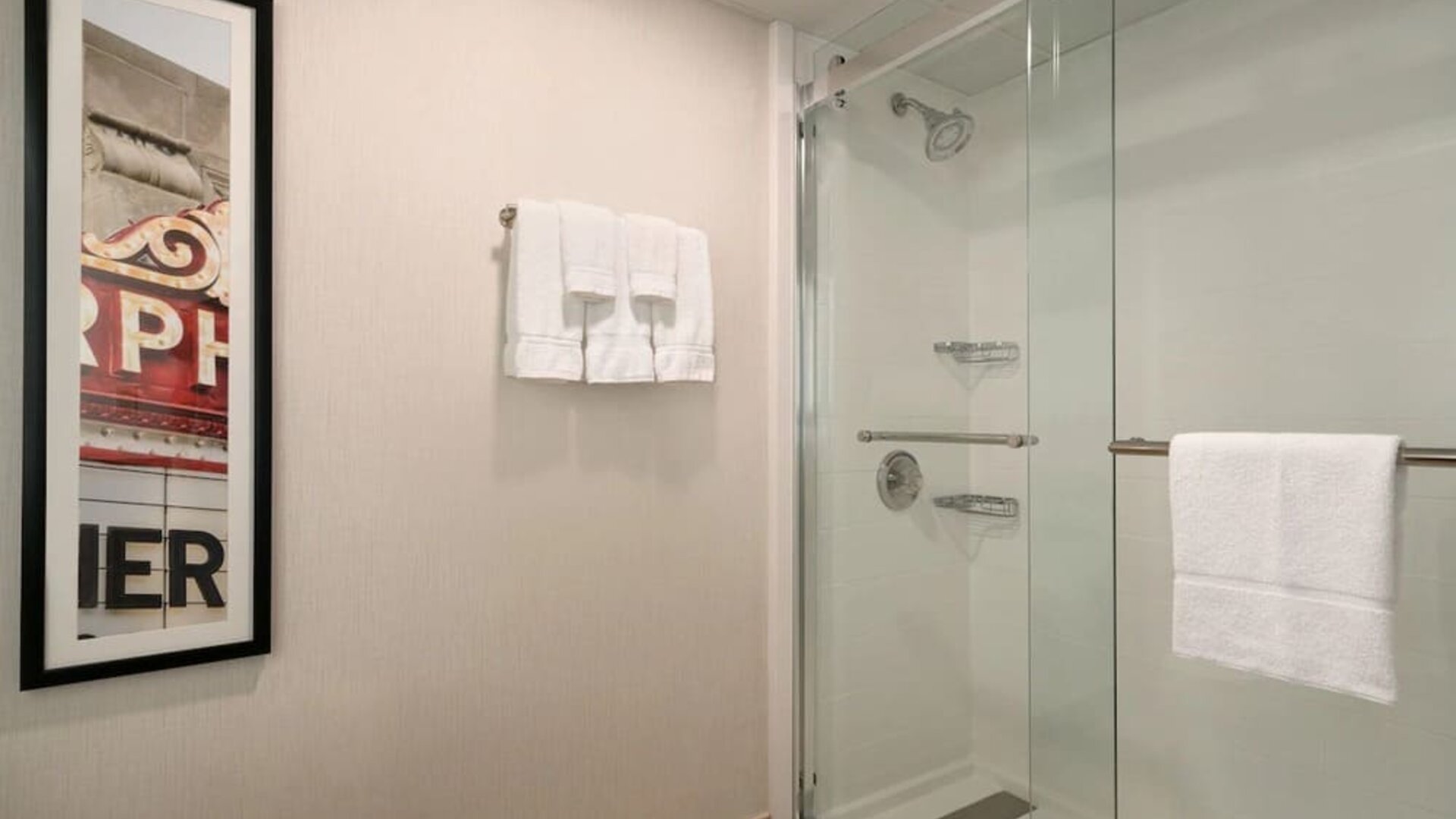 Guest bathroom featuring a glass-enclosed shower, wall-mounted showerhead, fresh towels, and contemporary décor. Crowne Plaza Englewood.