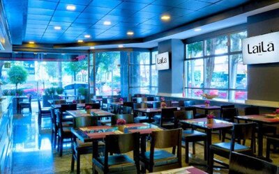 Stylish hotel lobby with black leather seating, mirrored walls and decorative overhead greenery. LaiLa Hotel CDMX.