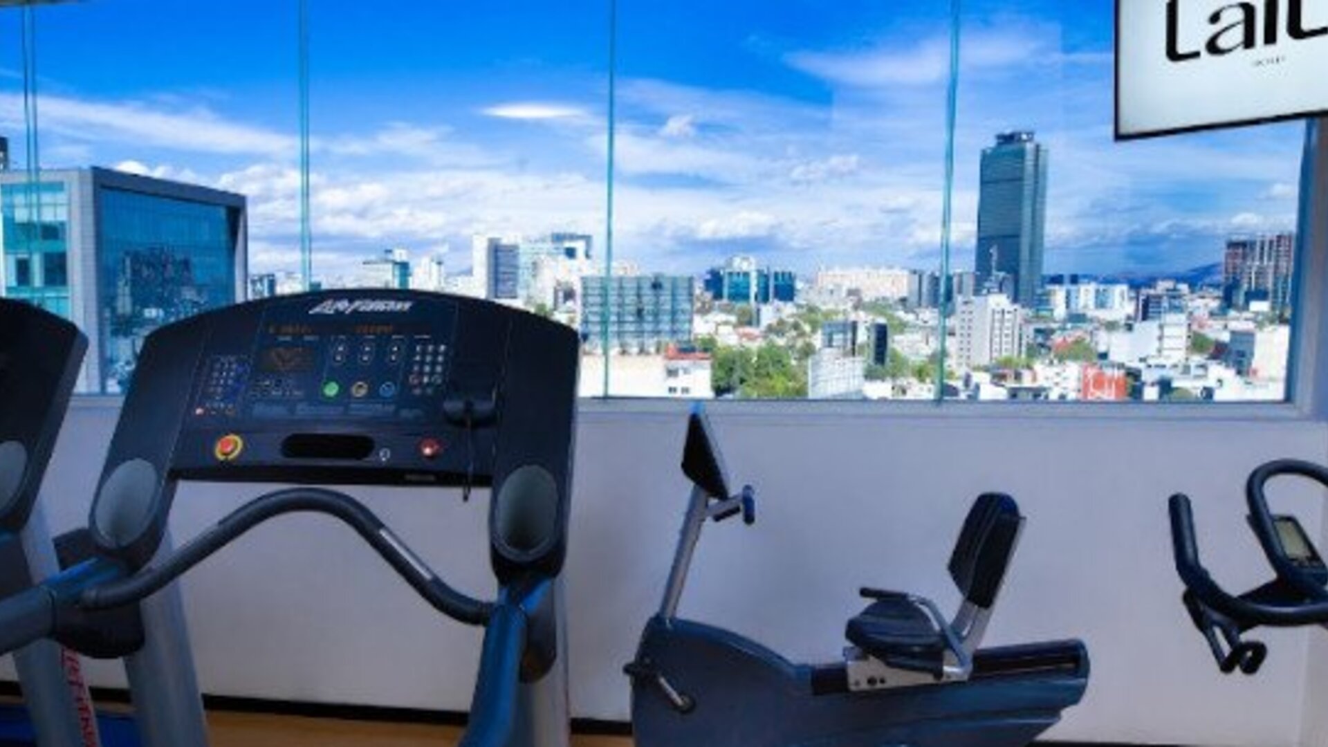Fitness centre featuring cardio equipment and large windows overlooking the Mexico City skyline. LaiLa Hotel CDMX.