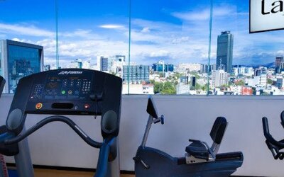 Fitness centre featuring cardio equipment and large windows overlooking the Mexico City skyline. LaiLa Hotel CDMX.