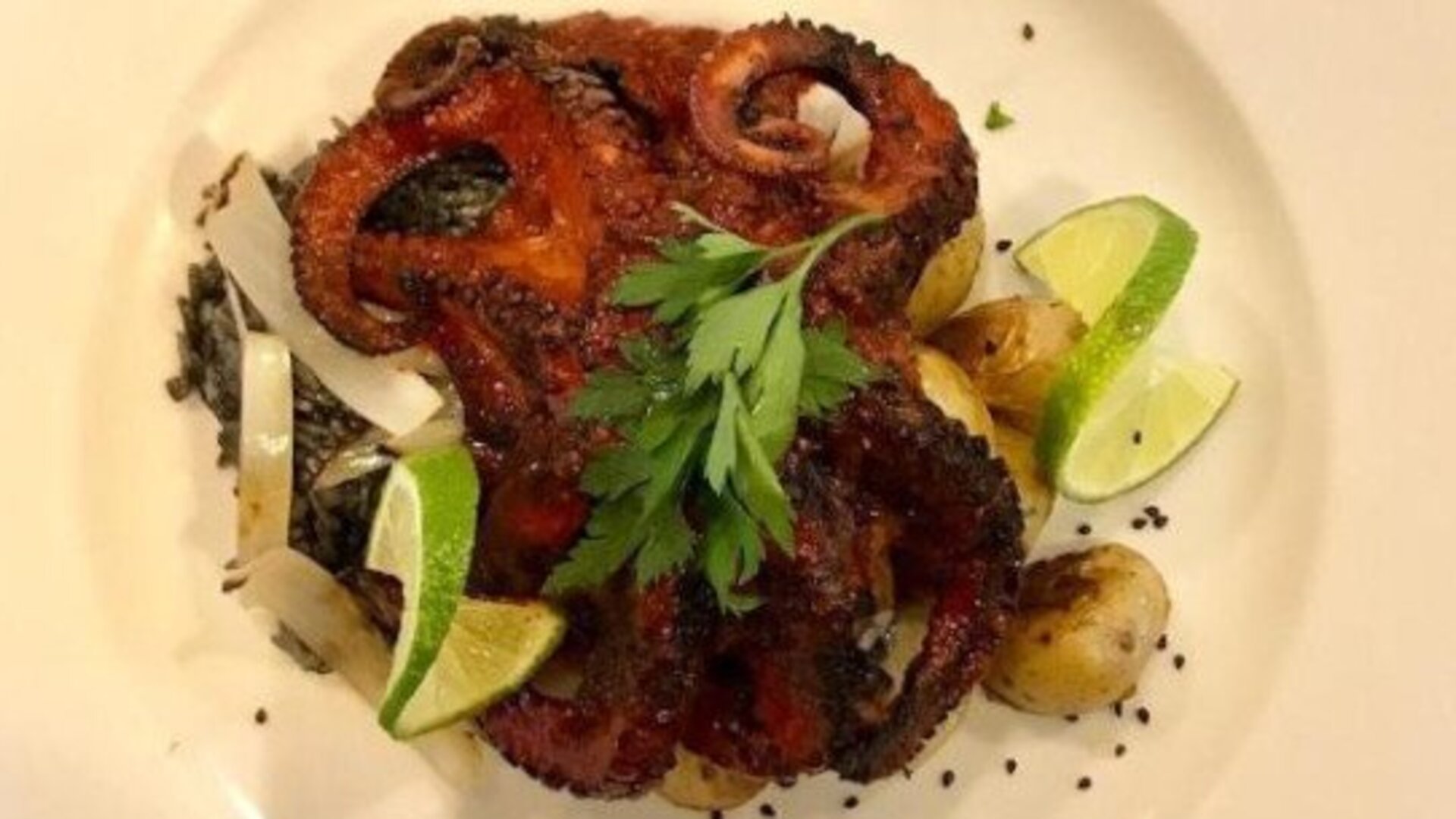 Grilled octopus dish served with lime wedges, roasted vegetables and fresh herbs. LaiLa Hotel CDMX.