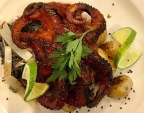 Grilled octopus dish served with lime wedges, roasted vegetables and fresh herbs. LaiLa Hotel CDMX.
