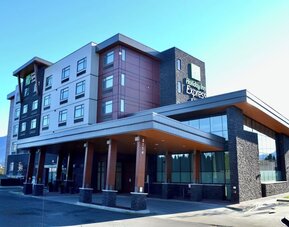 Modern Holiday Inn Express hotel exterior with a multi-story façade, covered entrance, large windows, stone accents, and mountain scenery in the distance.