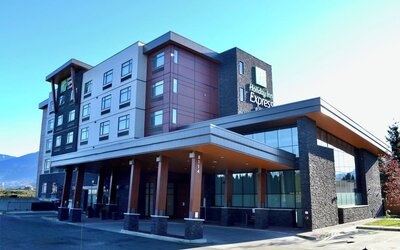 Modern Holiday Inn Express hotel exterior with a multi-story façade, covered entrance, large windows, stone accents, and mountain scenery in the distance.