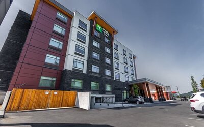 Exterior view of a modern Holiday Inn Express hotel with multi-story red, white, and dark stone façade, covered entrance, and adjacent parking area.