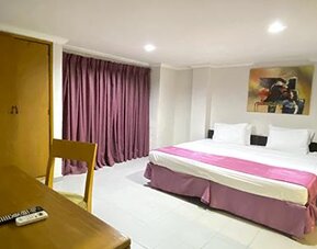 Spacious guest room with king bed, table, television and purple curtains at Hotel Puerta de Oro.