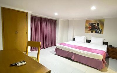 Spacious guest room with king bed, table, television and purple curtains at Hotel Puerta de Oro.