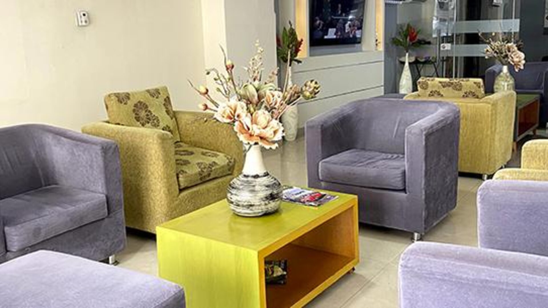 Lobby seating area with green and grey armchairs, coffee table and floral arrangement at Hotel Puerta de Oro.