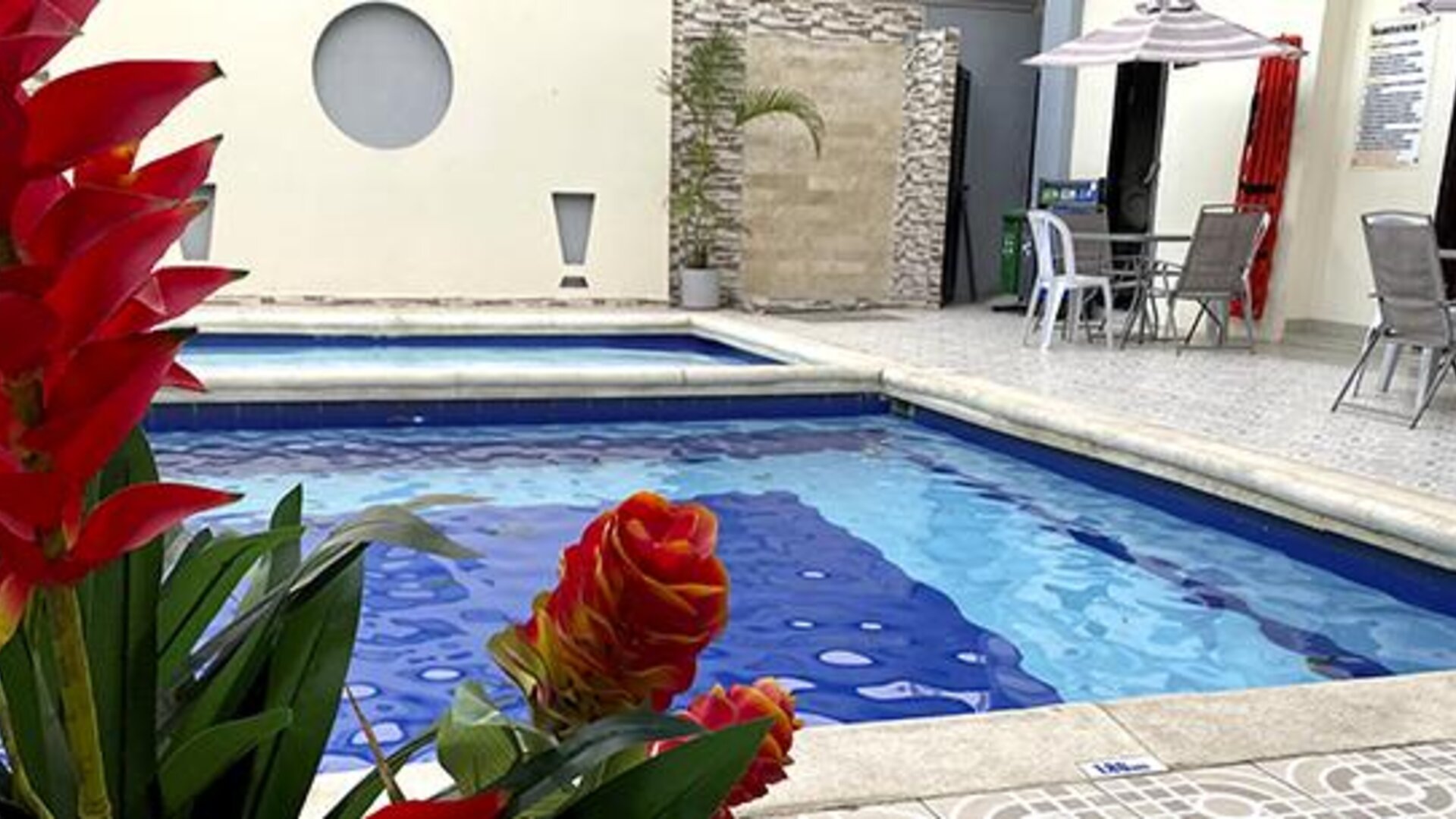 Outdoor swimming pool with tropical plants and patio seating at Hotel Puerta de Oro.